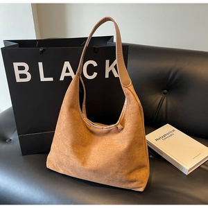 Détail du sac hobo en daim marron doux avec large bandoulière posé sur un canapé