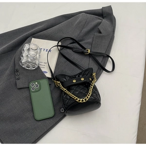 Detailed view of black quilted bucket bag with gold chain strap on grey blazer