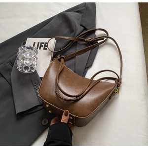 Detail of vintage brown hobo bag with metal rivet studs on a gray suit jacket