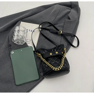 Detailed view of black quilted bucket bag featuring gold chain and diamond stitch texture