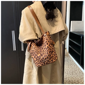 Close-up of leopard print bucket bag with brown leather strap worn with a beige coat