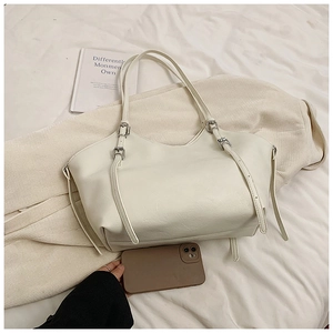 Detail view of cream tote bag with lychee texture, silver buckle, and smartphone for scale