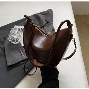 Detail of dark brown crescent bucket bag with glossy finish and knotted strap detail