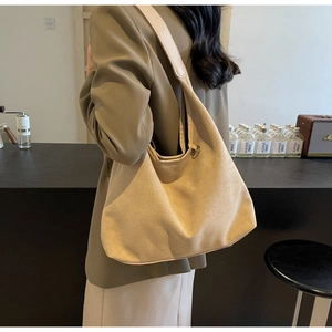 Détail du grand sac à bandoulière en daim beige porté par un mannequin en intérieur