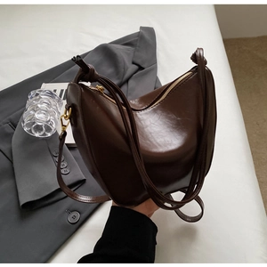 Detail of dark brown leather crescent bag featuring a knotted strap and gold zipper