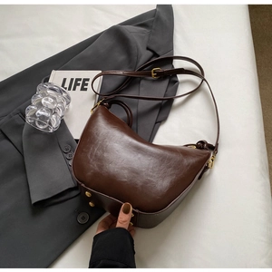 Detail of dark brown leather crescent bag with gold buckle on white fabric background