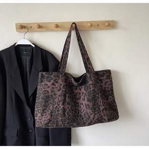 Close-up of leopard print tote bag hanging on wooden hook with black blazer