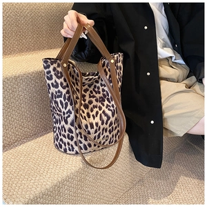 Detail of leopard print tote bag with brown leather handles and gold branding on suede