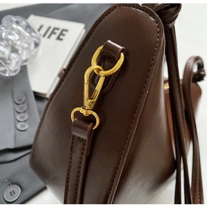 Close-up of shiny gold lobster clasp hardware on a dark brown leather bucket bag