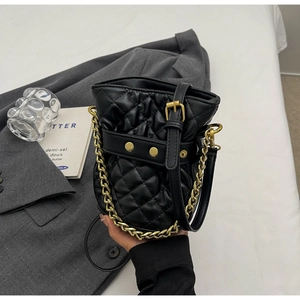 Detailed view of black quilted bucket bag with gold chain handle and leather strap