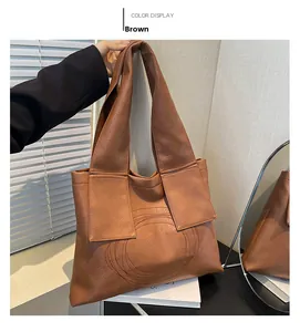 Close-up of a brown leather shoulder bag featuring circular stitching and wide straps