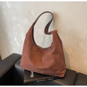 Détail d'un grand sac à épaule en daim marron posé sur un meuble en cuir avec magazine