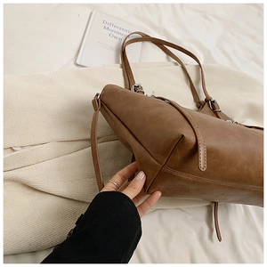 Close-up of brown PU leather tote bag showing side strap detail and metallic buckle