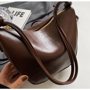 Close-up of a retro brown oil-wax leather bucket bag with golden zipper and slim straps