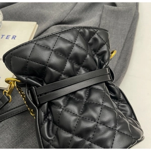 Close-up of quilted black leather bucket bag with gold chain and metal ring details