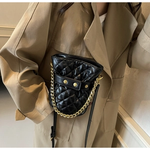 Macro shot of quilted black bucket bag with gold chain strap on a trench coat