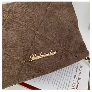 Close-up of quilted brown suede texture with star stitching and a gold logo detail