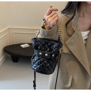 Detail of black quilted bucket bag with gold chain handle and stud closure strap