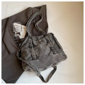 Detail of grey washed denim tote bag with wide straps and metal hardware on blazer