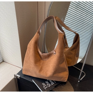 Détail du sac hobo en daim caramel avec poignée lisse et anneau sur surface sombre