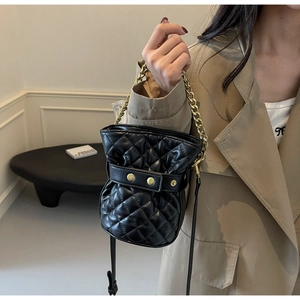 Close-up of quilted black bucket bag with gold chain strap and metallic studs on leather