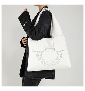 Modern white tote bag with black circular stitching shown on a model's shoulder