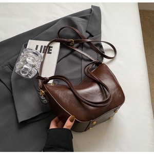 Detailed view of dark brown crescent bag with gold metal studs and sleek leather finish