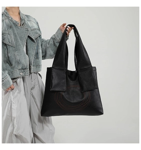 Detail of black tote bag featuring red circular embroidery and pebbled leather texture