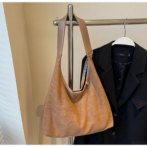 Détail du sac hobo en daim marron souple avec large bandoulière suspendu à un cintre