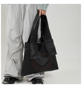 Detail of black pebbled leather tote bag with red spiral totem and wide shoulder strap