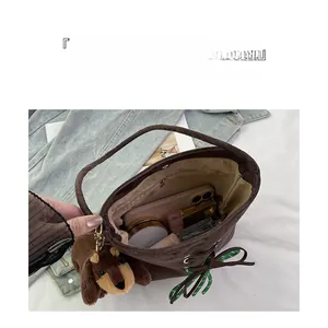 Detail of spacious dark brown suede bucket bag with green polka dot ribbon and plush charm