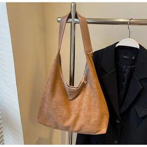 Gros plan détaillé sur le sac hobo en daim marron et sa large bandoulière en cuir sur support