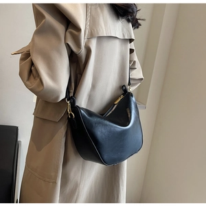 Detail of black faux leather half-moon shoulder bag styled with khaki trench coat