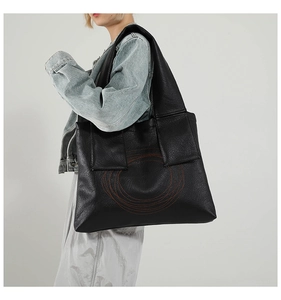 Detail of large black tote bag featuring distinctive orange spiral stitching and wide straps