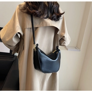 Modern black crescent shoulder bag with golden hardware shown on a trench coat model