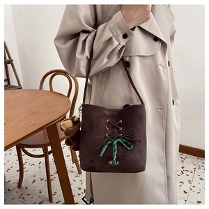 Detail of dark brown suede bucket bag with green woven rope and teddy bear charm