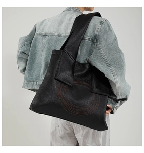 Close-up of a large black tote bag with orange spiral stitching on textured leather