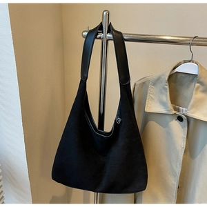 Détail du sac cabas en daim noir avec bandoulière en cuir sur un support en métal