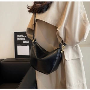 Detailed view of a black crescent shoulder bag in matte faux leather with gold buckles