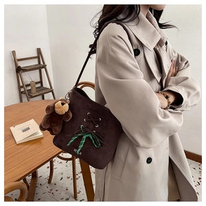 Close-up of brown suede bucket bag featuring a plaid bow and a plush bear charm detail