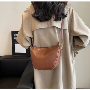 Detail of caramel brown crossbody bag with gold zipper and leather strap on model