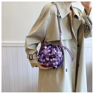 Dettaglio di una borsa a secchiello con paillettes viola e coulisse su cappotto beige