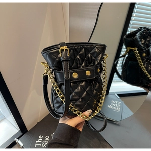 Close-up of quilted black bucket bag with gold chain handle and polished studs
