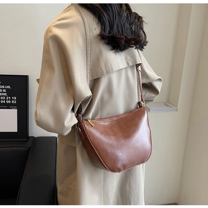 Detail of dark brown leather crescent bag with adjustable strap on a neutral trench coat