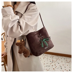 Detail of suede bucket bag with decorative bow tie and plush puppy charm on model