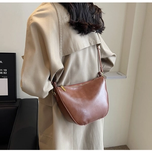 Close-up of a brown leather crescent shoulder bag paired with an elegant beige trench coat