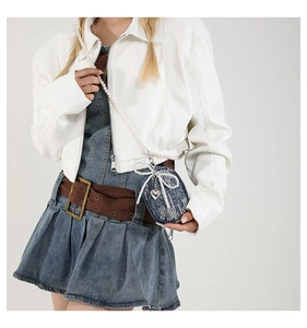 Détail d'un mini sac en denim bleu avec nœud en perles et pendentif cœur sur veste