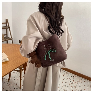 Detail of dark brown suede bucket bag with cross-lace decor and green plaid bow