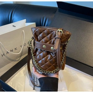 Detail of brown quilted bucket bag with gold chain strap on a black leather sofa