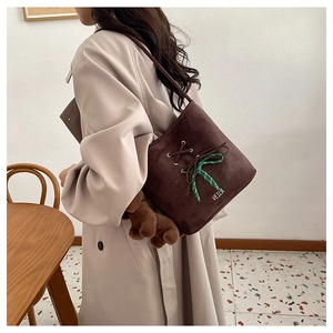 Close-up of brown suede bucket bag with ribbon bow, bear charm, and logo detail